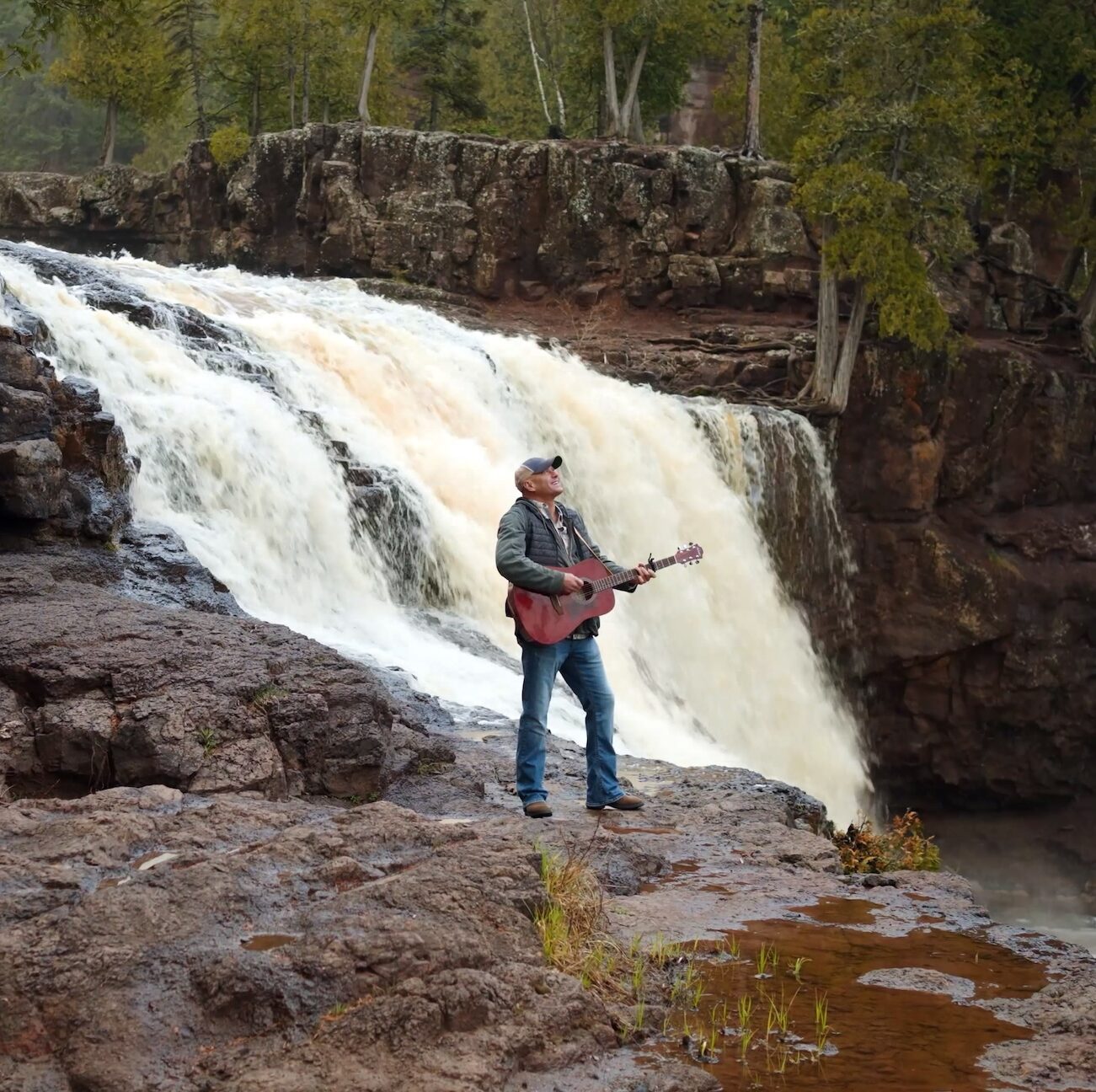 Brian Leighton playing a guitar in front of Gooseberry Falls, MN.