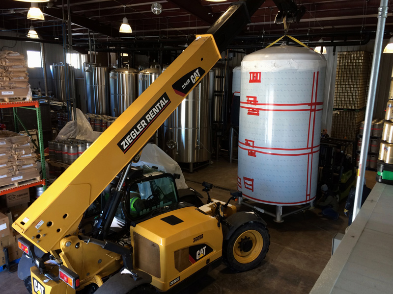 Crane lifting a new tank into place in a brewery.